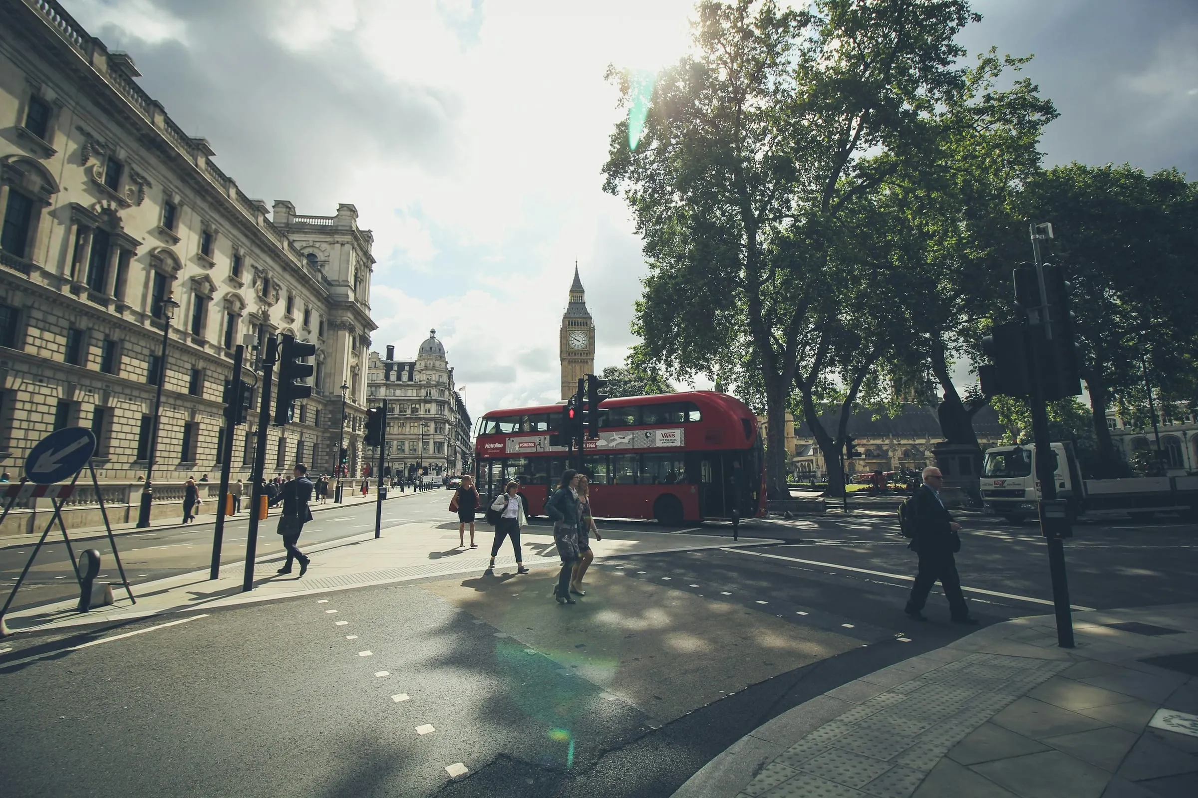 People crossing a street in Westminster, with a red bus and Big Ben behind